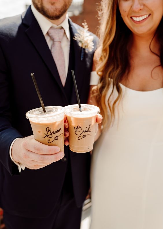 groom and bride hold iced coffee and pose for a picture