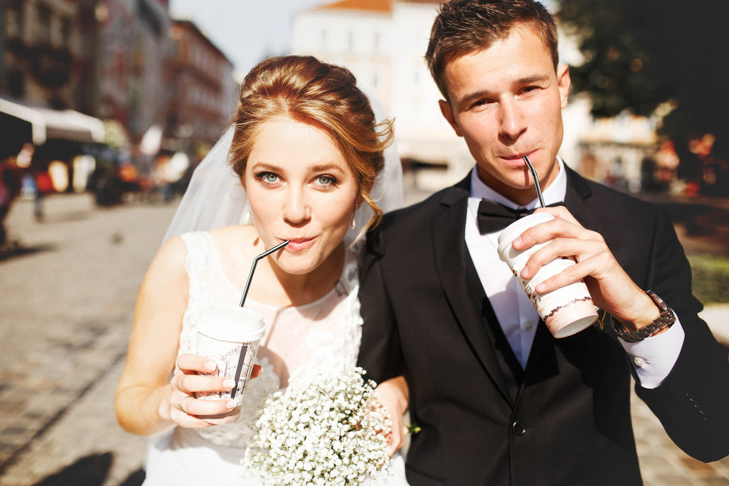couple poses while drinking iced coffee in a town square