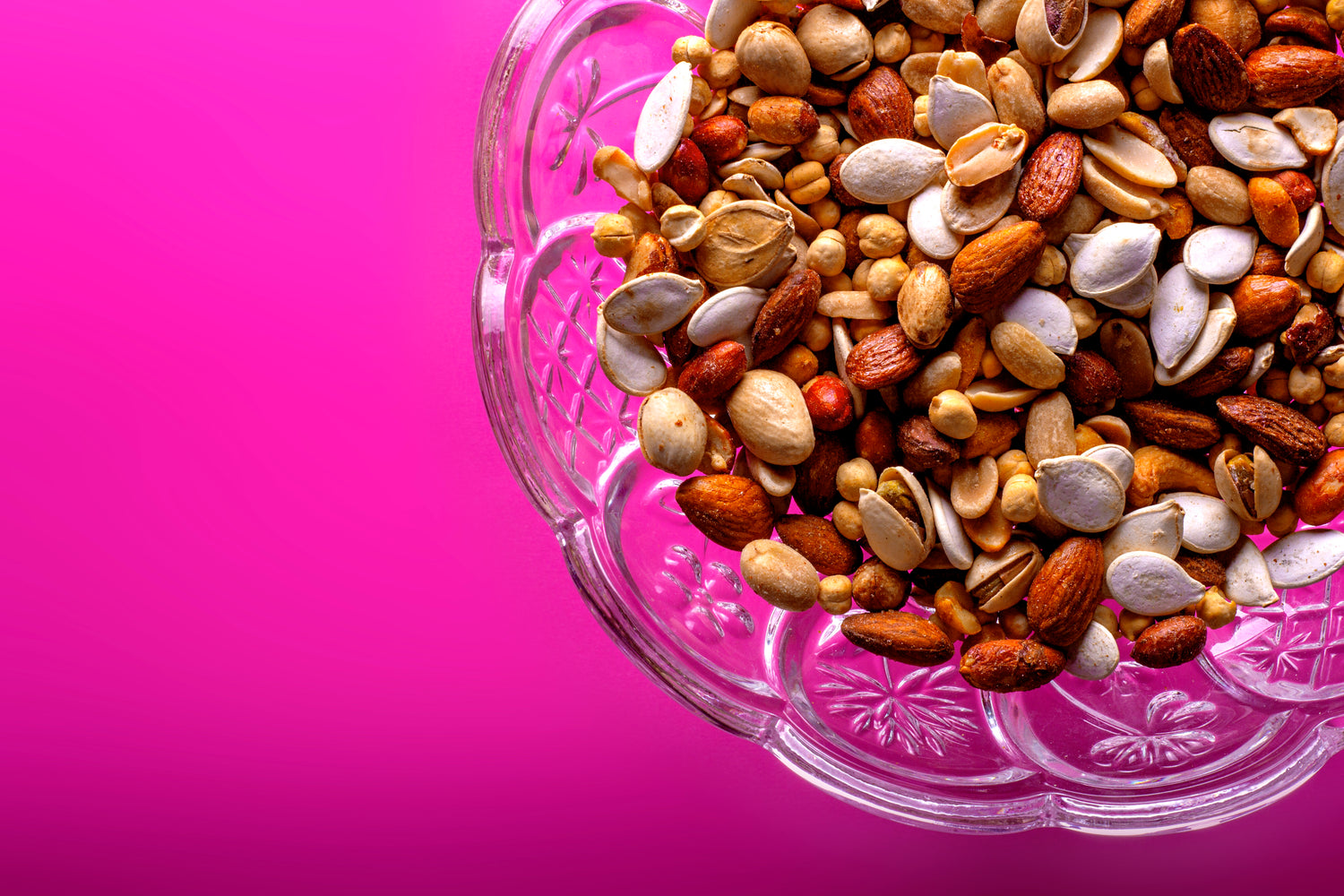 mixed nuts in a glass bowl on pink paper table runner